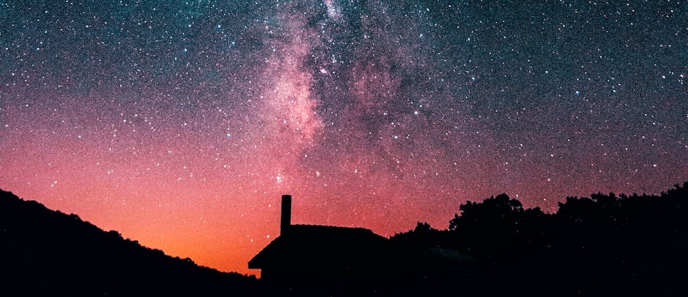A silhouette of a solitary house beneath the Milky Way.