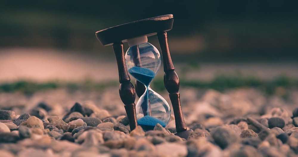 An hourglass containing blue sand, resting on pebbles