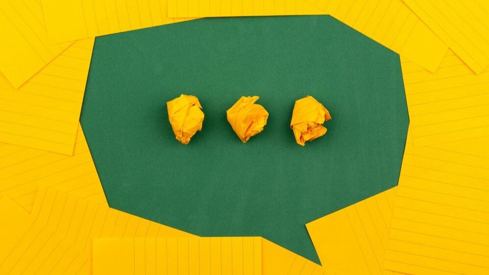 A green speech bubble made of card, surrounded by sheets of yellow paper.