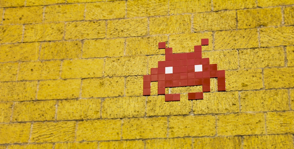 A retro Space Invader made of small red tiles on a yellow brick wall.