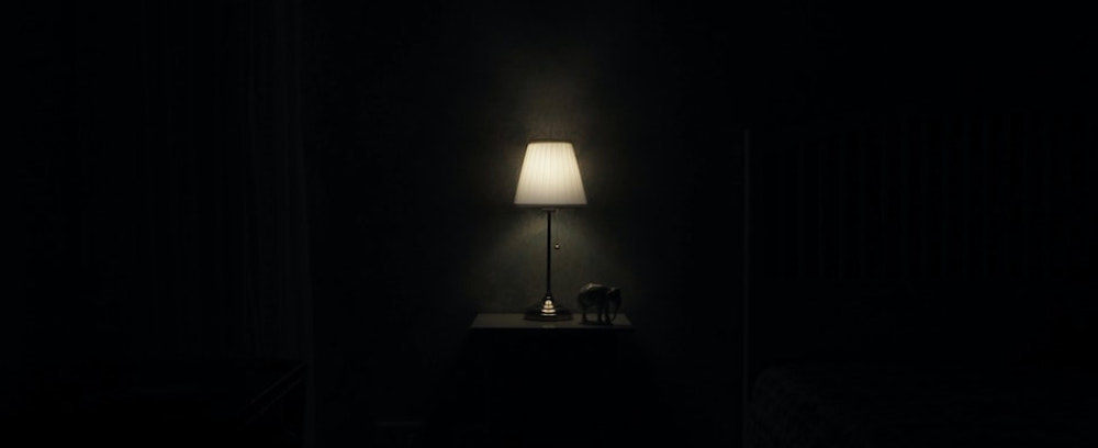 A pitch black room barely illuminated by a solitary desk lamp.