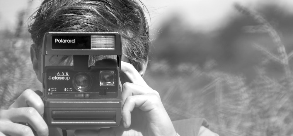 A young man holding a vintage Polaroid camera.
