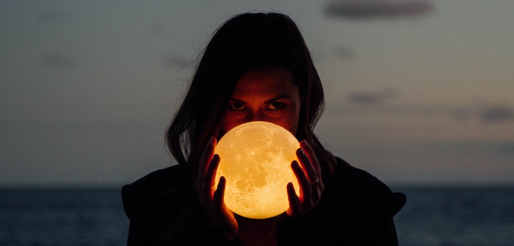 A woman holding a shining moon in her hands